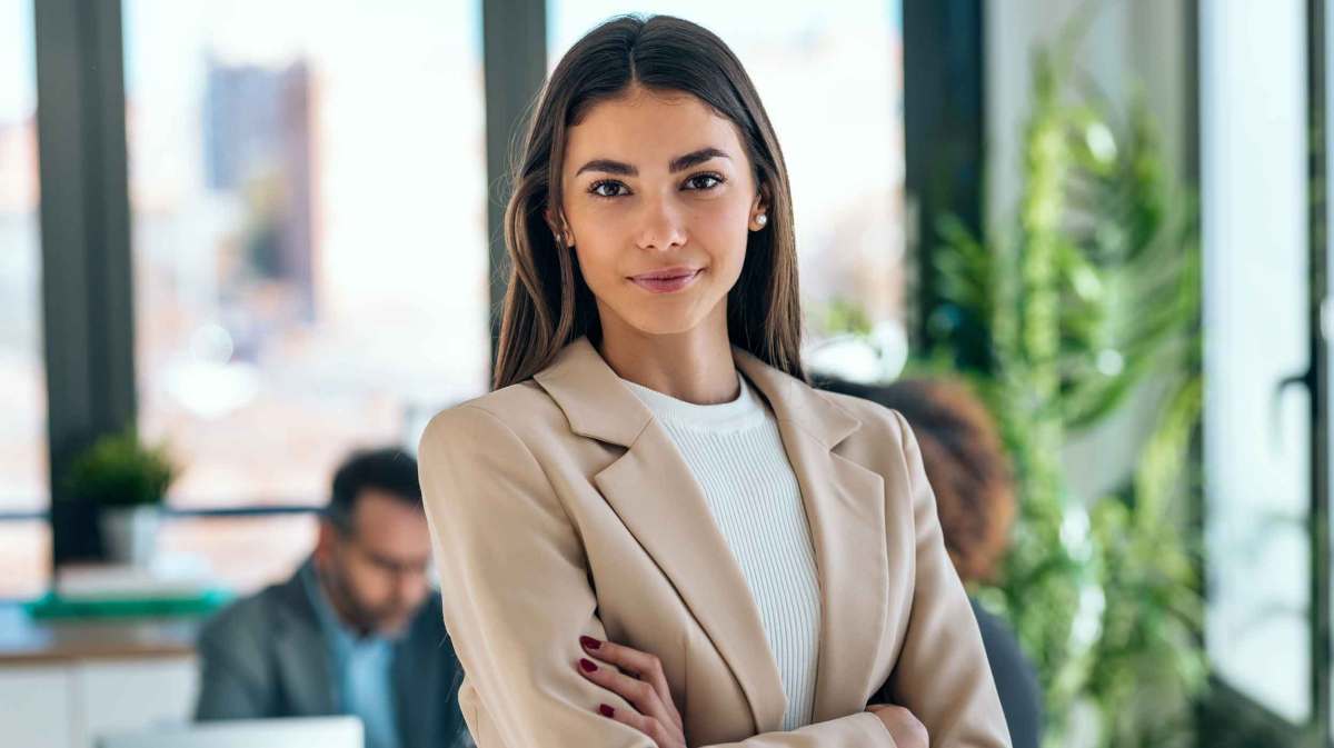 Frau steht selbstbewusst mit verschränkten Armen im Büro.