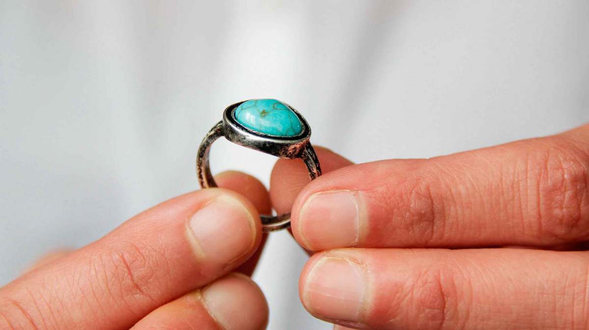 Mann hält einen großen Ring mit einem türkisfarbenen Stein in der Hand.