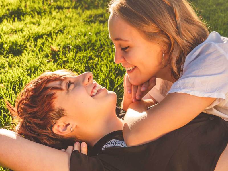 Verliebtes lesbisches Pärchen liegt auf dem Gras. Eine der beiden liegt mit ihrem Oberkörper auf dem der anderen.