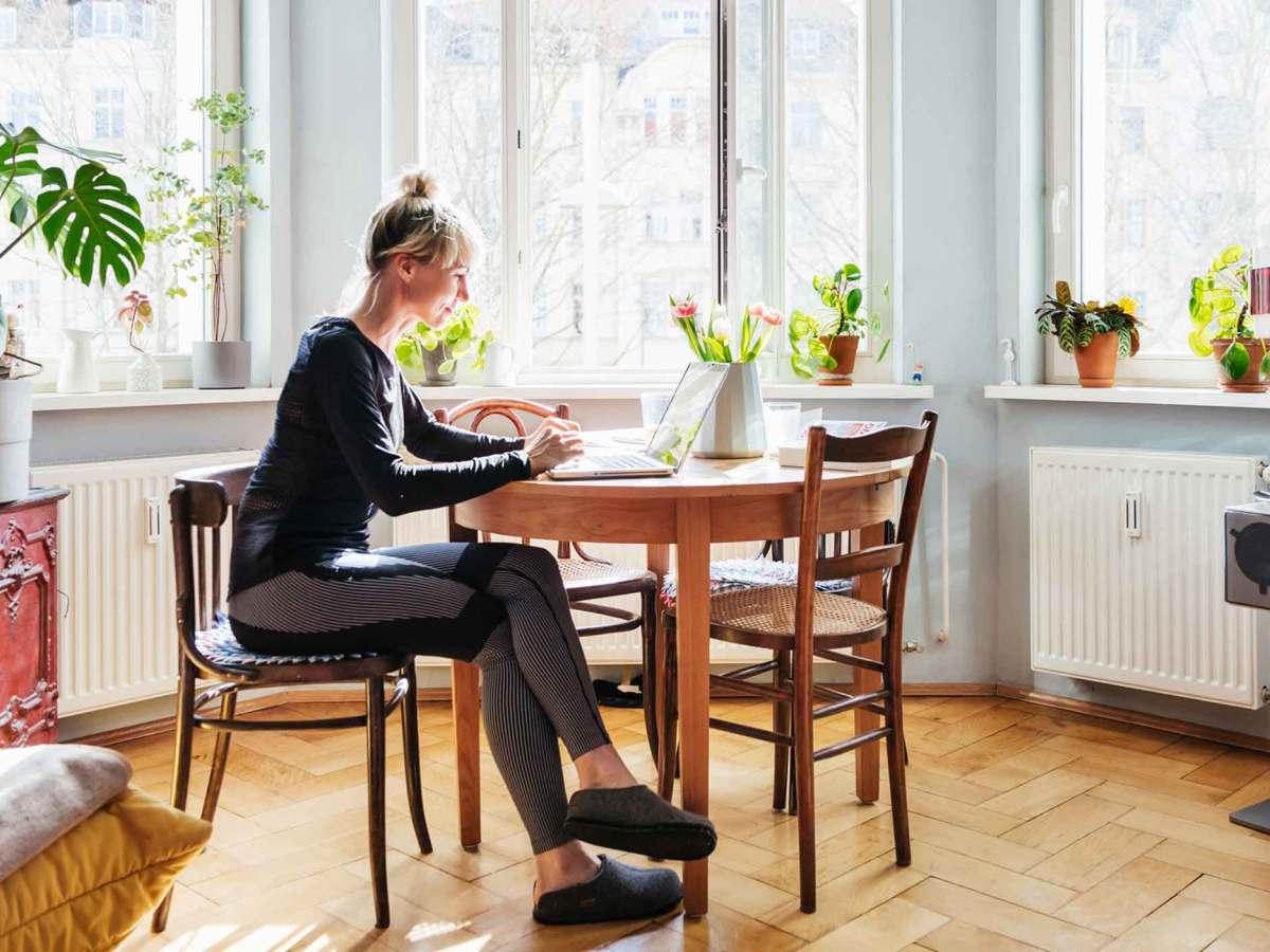 Frau sitzt in beqeuemer Kleidung zu Hause im Homeoffice am K&uuml;schentisch.