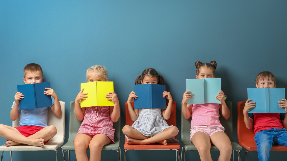Kinder mit Büchern sitzen vor einer blauen Wand auf Stühlen