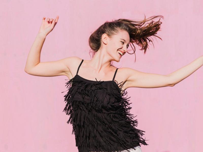 Frau mit schwarzem Top tanzt vor einer pinken Wand.