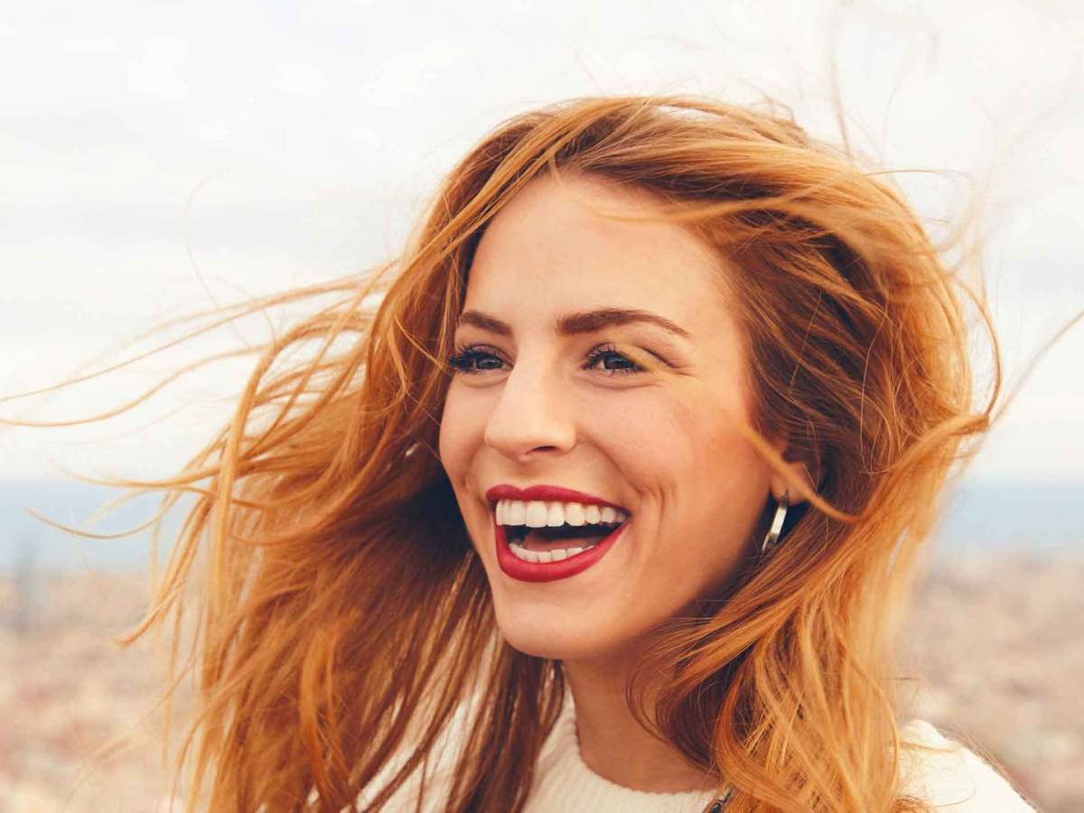 Lachende junge Frau steht drau&szlig;en und lacht laut.