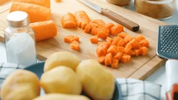 Gekochte Möhren, gewürfelt. Zubereitung eines Gemüsesalats namens Vinaigrette. Küchenmesser auf einem Schneidebrett zum Schneiden von Gemüse. In der Nähe befinden sich weitere Zutaten. Das Konzept der vegetarischen und veganen Ernährung.