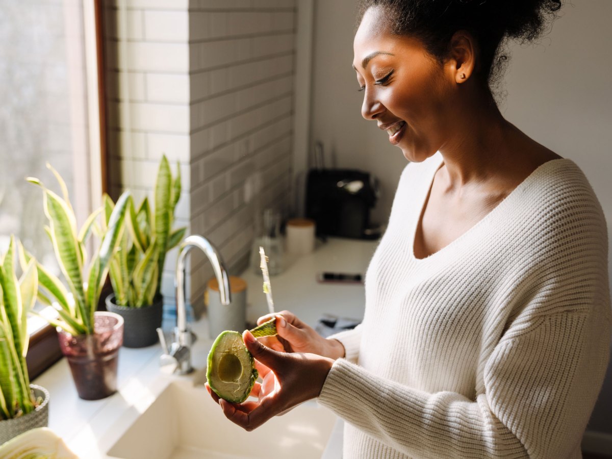 Erwachsene schöne afrikanische lächelnde schwangere Frau schält Avocado