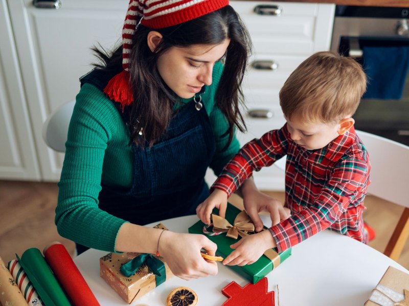 Mutter und Sohn packen zusammen Weihnachtsgeschenke ein.