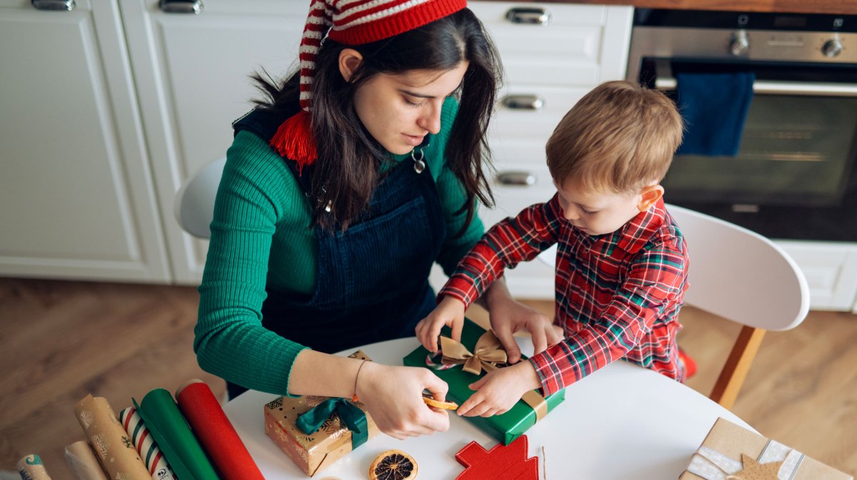 Mutter und Sohn packen zusammen Weihnachtsgeschenke ein.