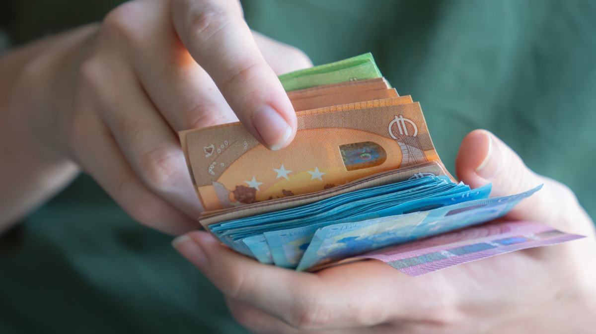 Eine Hand zählt einen dicken Stapel Euro-Geldscheine in verschiedenen Farben, mit Fokus auf einen 50-Euro-Schein.