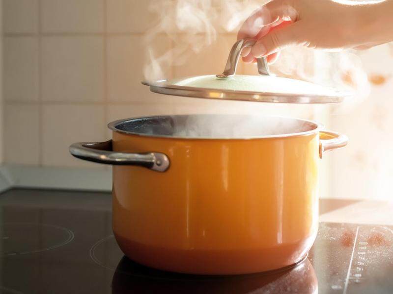 Frau hebt den Deckel von einem Kochtopf, der dampft.