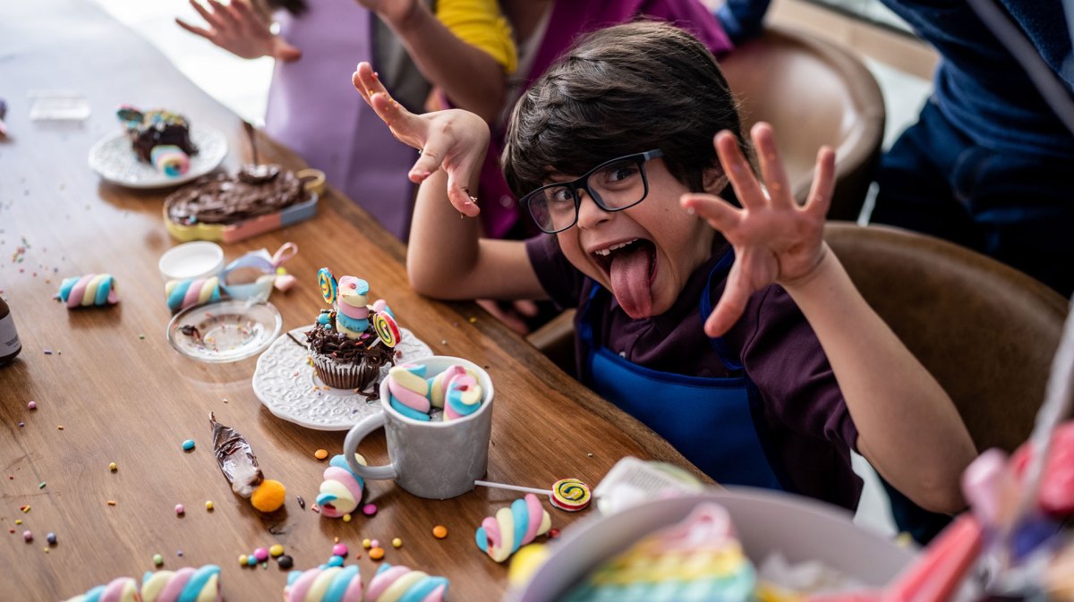 Porträt eines Jungen, der an einem Kindergeburtsag zu Hause mit Süßigkeiten spielt und eine lustige Grimasse zieht.