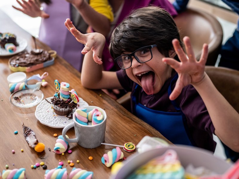 Porträt eines Jungen, der an einem Kindergeburtsag zu Hause mit Süßigkeiten spielt und eine lustige Grimasse zieht.