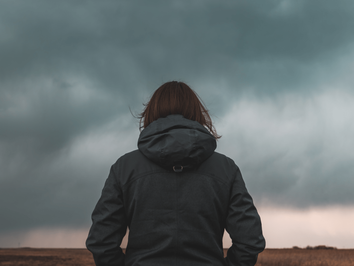 Frau steht mit dem R&uuml;cken zur Kamera vor einem d&uuml;steren Wolkenhimmel