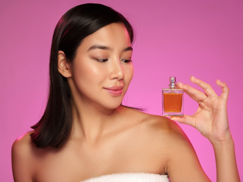 Frau vor pinkem Hintergrund, die ein Parfum in der Hand hält