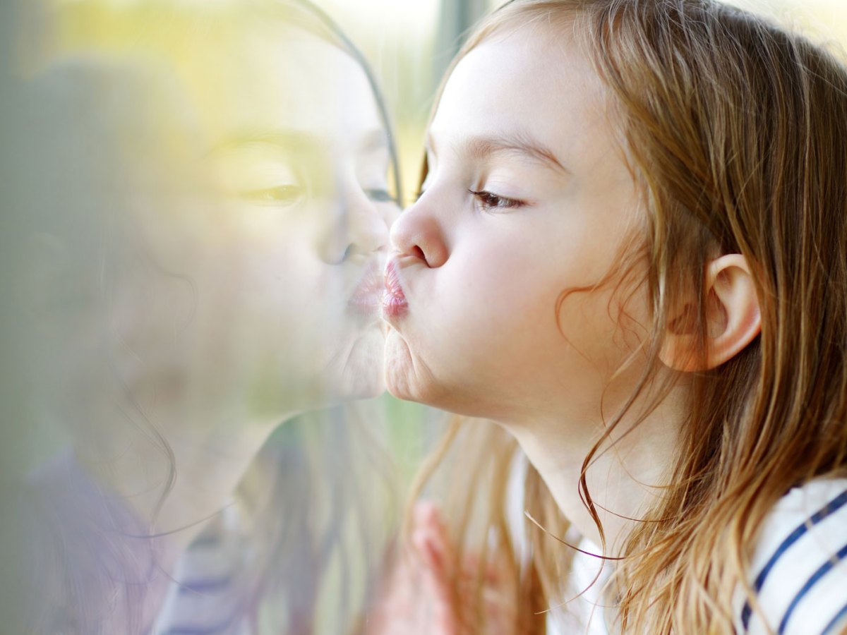 M&auml;dchen dr&uuml;ckt Nase und Mund an das Fenster.