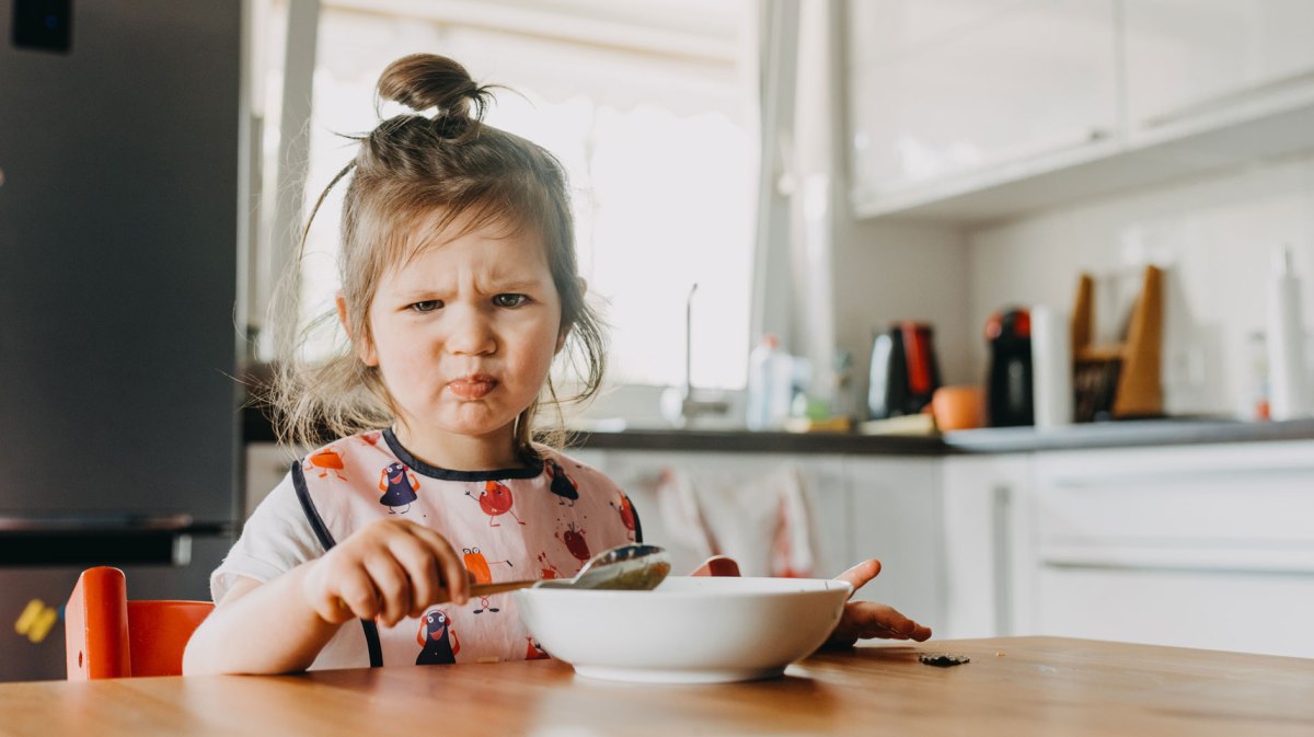Süßes, kleines Mädchen, das ein witziges Gesicht zieht beim Essen.