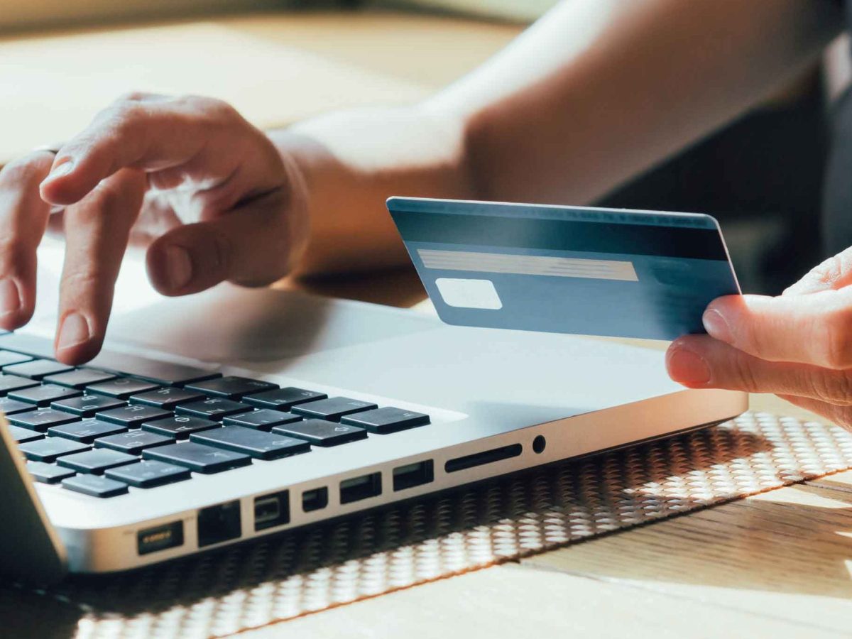 Frau tippt mit einer Hand auf dem Laptop und h&auml;lt in der anderen Hand ihre Bankkarte.