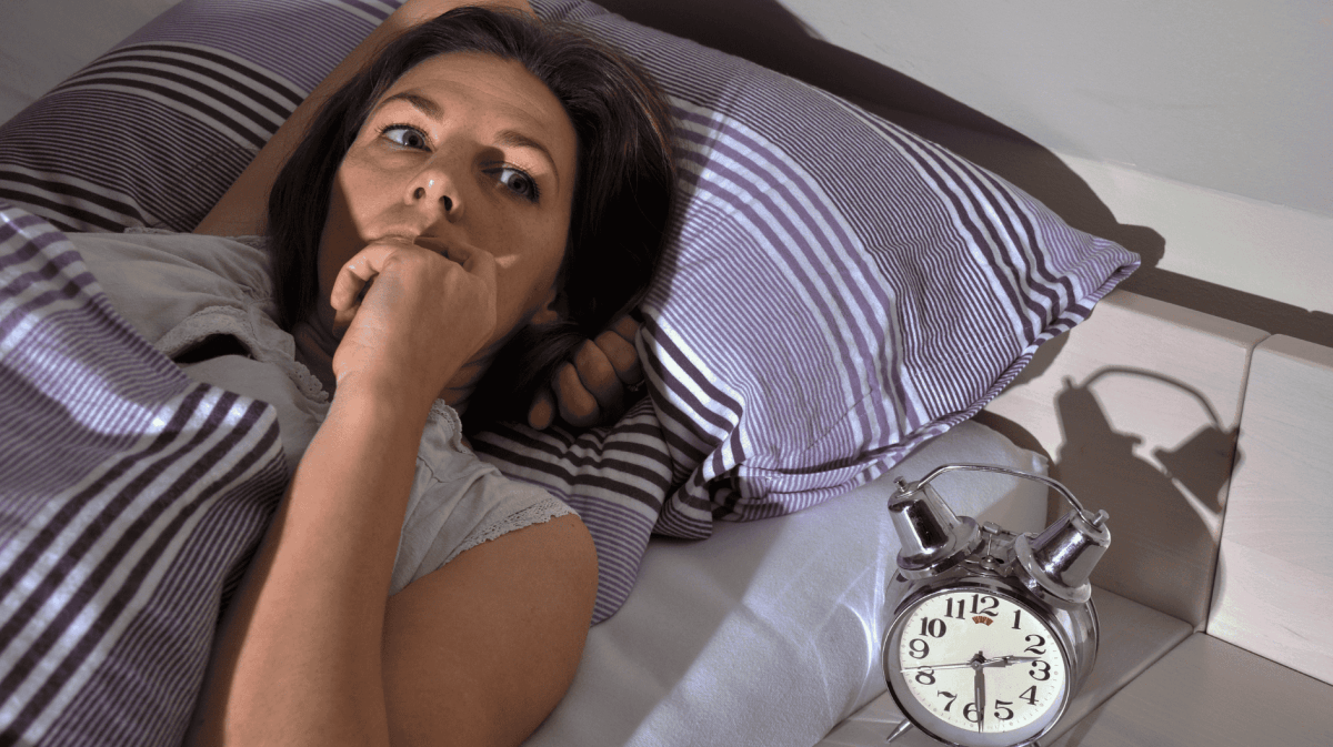 Frau liegt wach im Bett Mond scheint ins Zimmer, neben ihr steht ein Wecker der 02:30 Uhr zeigt