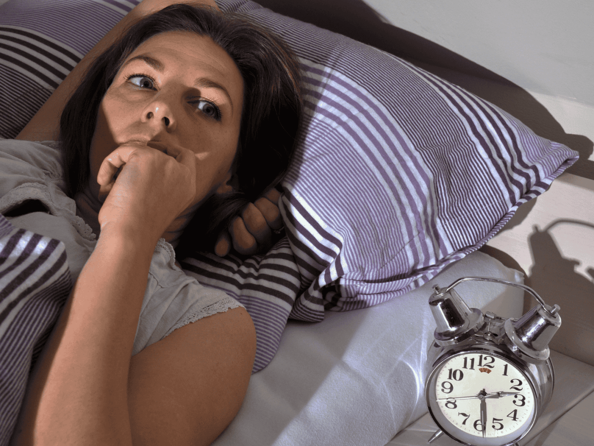 Frau liegt wach im Bett Mond scheint ins Zimmer, neben ihr steht ein Wecker der 02:30 Uhr zeigt