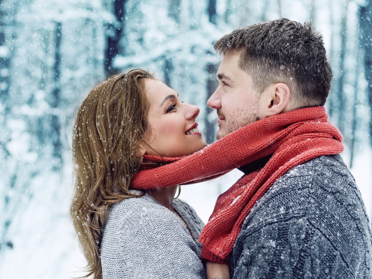 Frau und Mann in verschneitem Wald l&auml;cheln sich an