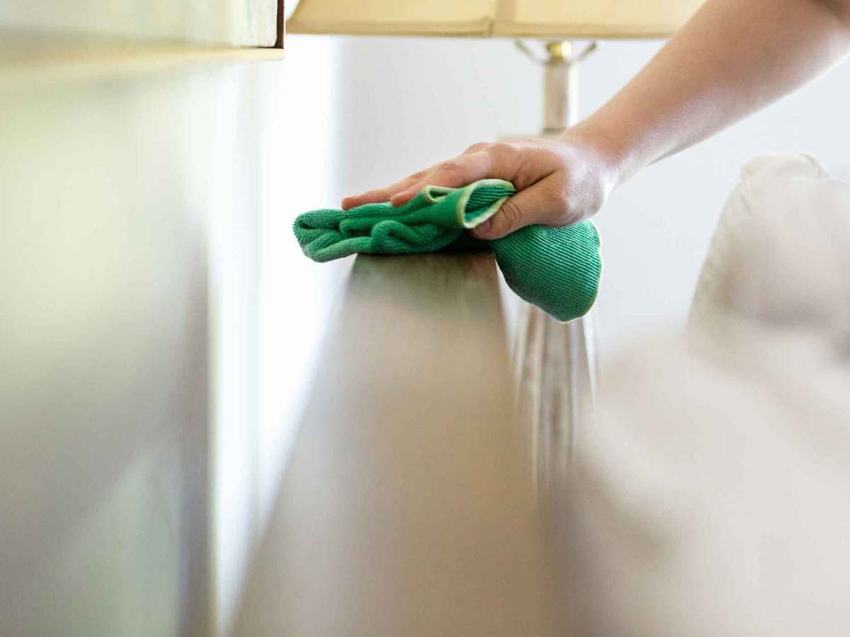 Frau wischt im Schlafzimmer Staub.