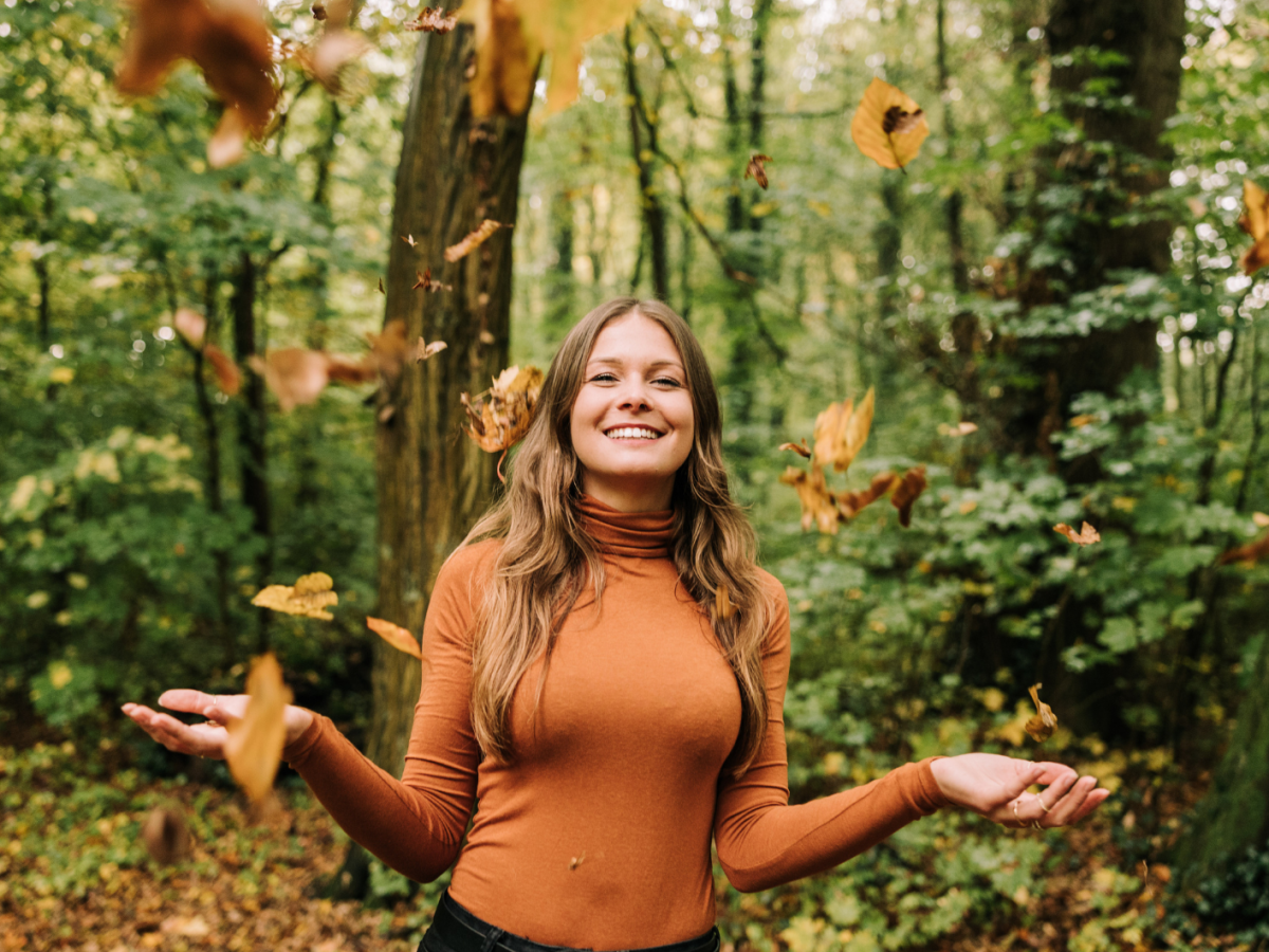 Frau im Wald, die lacht und Bl&auml;tter in die Luft wirft.