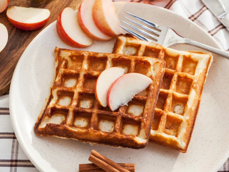 Waffeln auf einem weißen Teller mit Apfelscheiben darauf.
