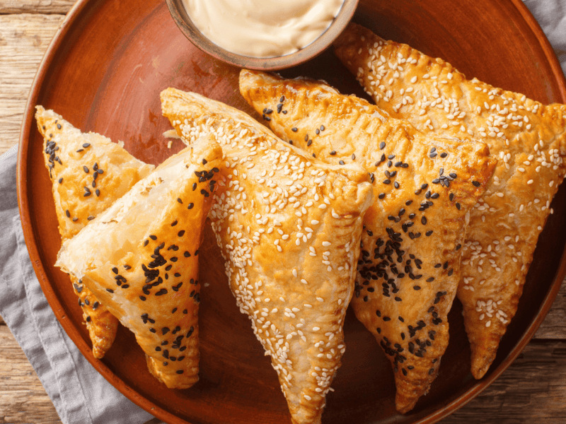 Blätterteigtaschen mit Sesam auf einem roten Teller.
