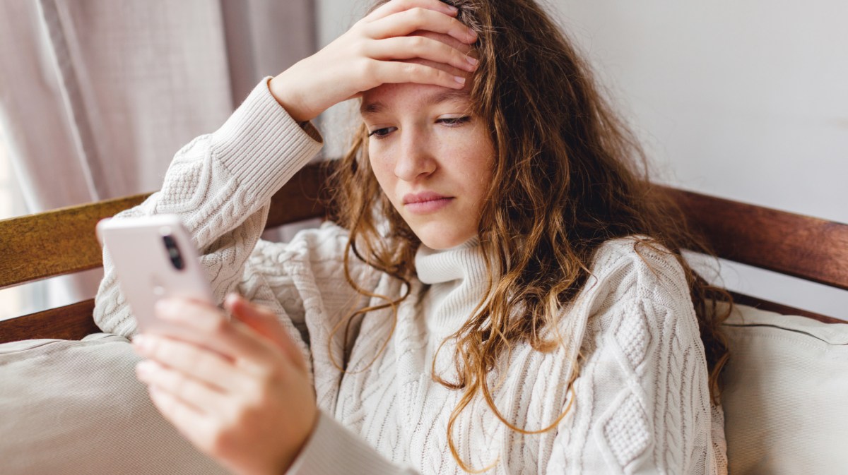 Junge Frau schaut nachdenklich auf ihr Handy.