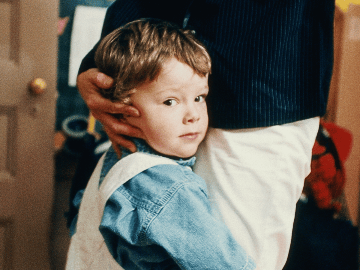 Kind umarmt die Beine einer Frau bei der Verabschiedung in der Kita.