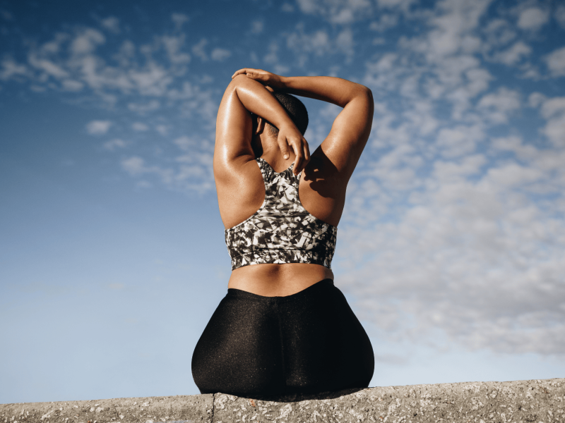 Plus size Frau sitzt auf einer Mauer und streched die Arme