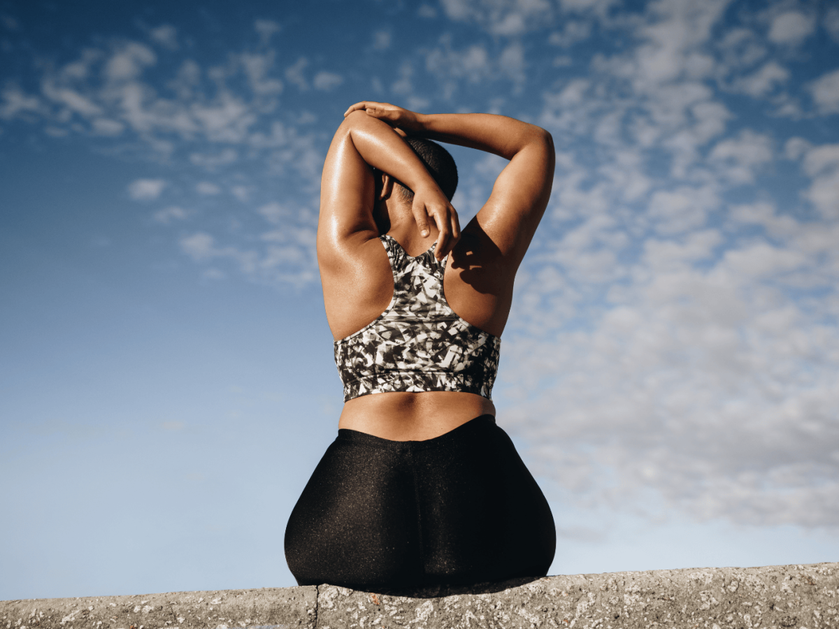 Plus size Frau sitzt auf einer Mauer und streched die Arme