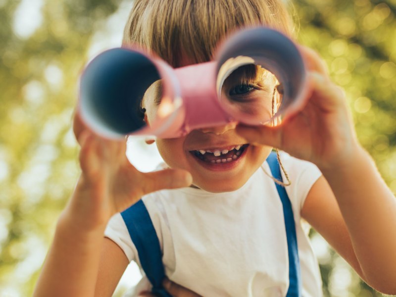 Nahaufnahme eines Kindes, das sich aus Toilettenpapierrollen ein Fernrohr gebaut hat und hindurchschaut.