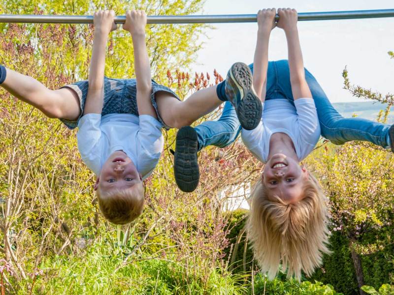 Zwei Kinder im Grundschulalter baumeln an einer Kletterstange mit dem Kopf nach unten.