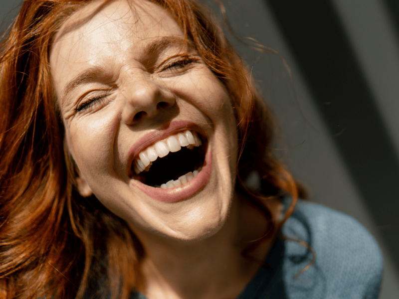 Junge Frau mit roten Haaren lacht ausgelassen.