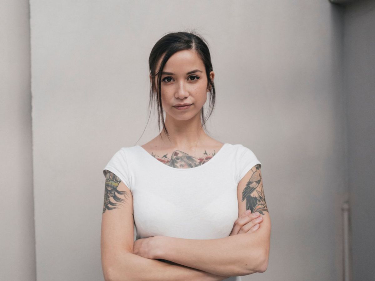 Frau mit Tattoos, verschr&auml;nkten Armen und wei&szlig;em Shirt ist stur.,