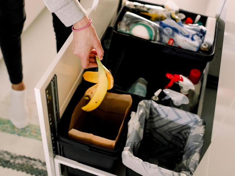 Frau wirft eine Bananenschale in einen Mülleimer in der Küche.