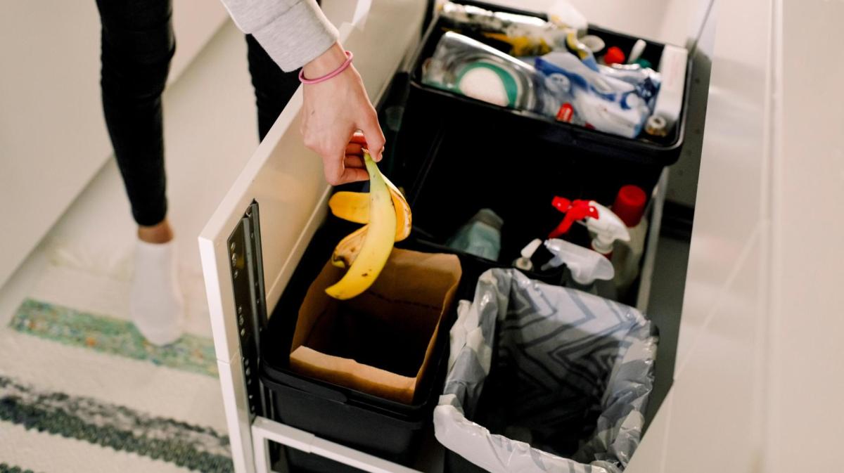 Frau wirft eine Bananenschale in einen Mülleimer in der Küche.