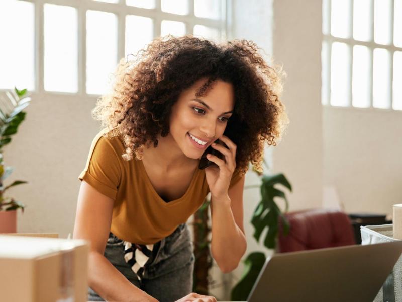 Frau telefoniert mit einem Handy und steht am Schreibtisch.