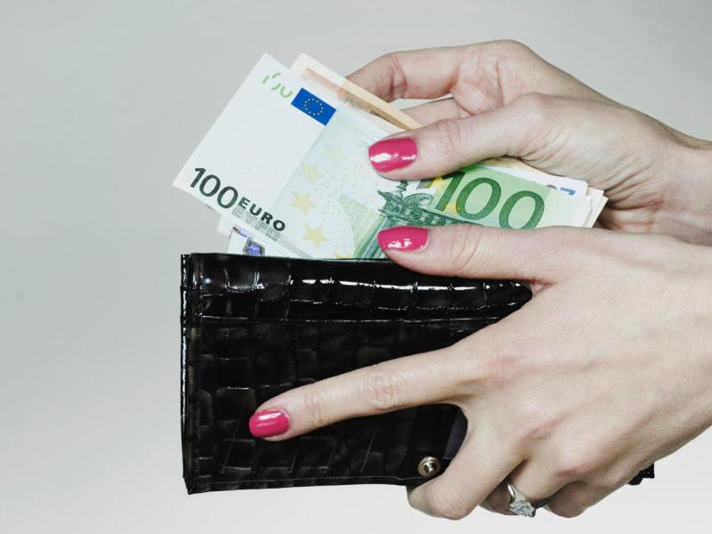 Frau legt Geldscheine in ein dunkles Portemonnaie.