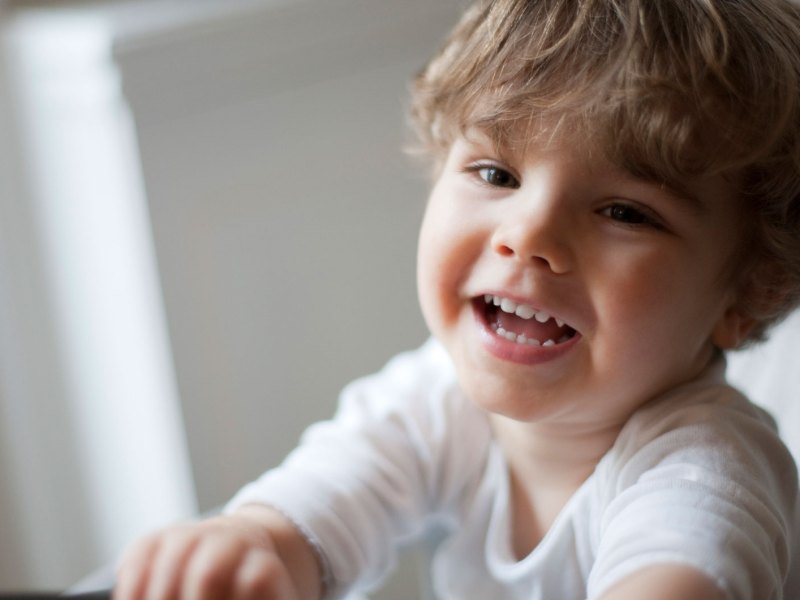 Nahaufnahme eines Dreijährigen im Stuhl, der an der Kamera vorbei lacht.