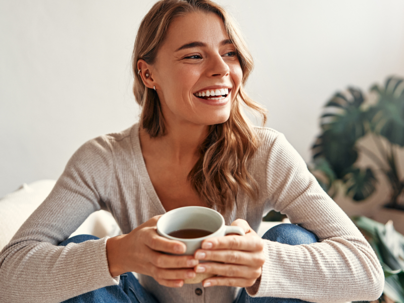 Junge Frau sitzt mit einem Tee in der Hand auf dem Sofa