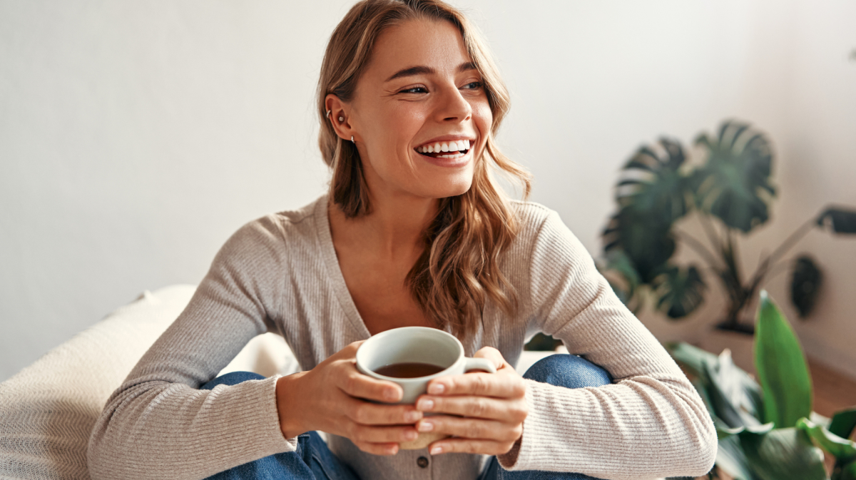 Junge Frau sitzt mit einem Tee in der Hand auf dem Sofa