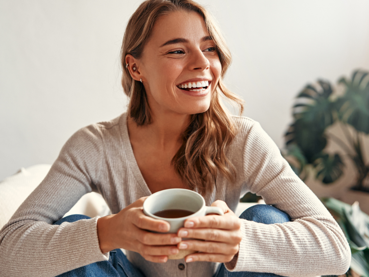 Junge Frau sitzt mit einem Tee in der Hand auf dem Sofa