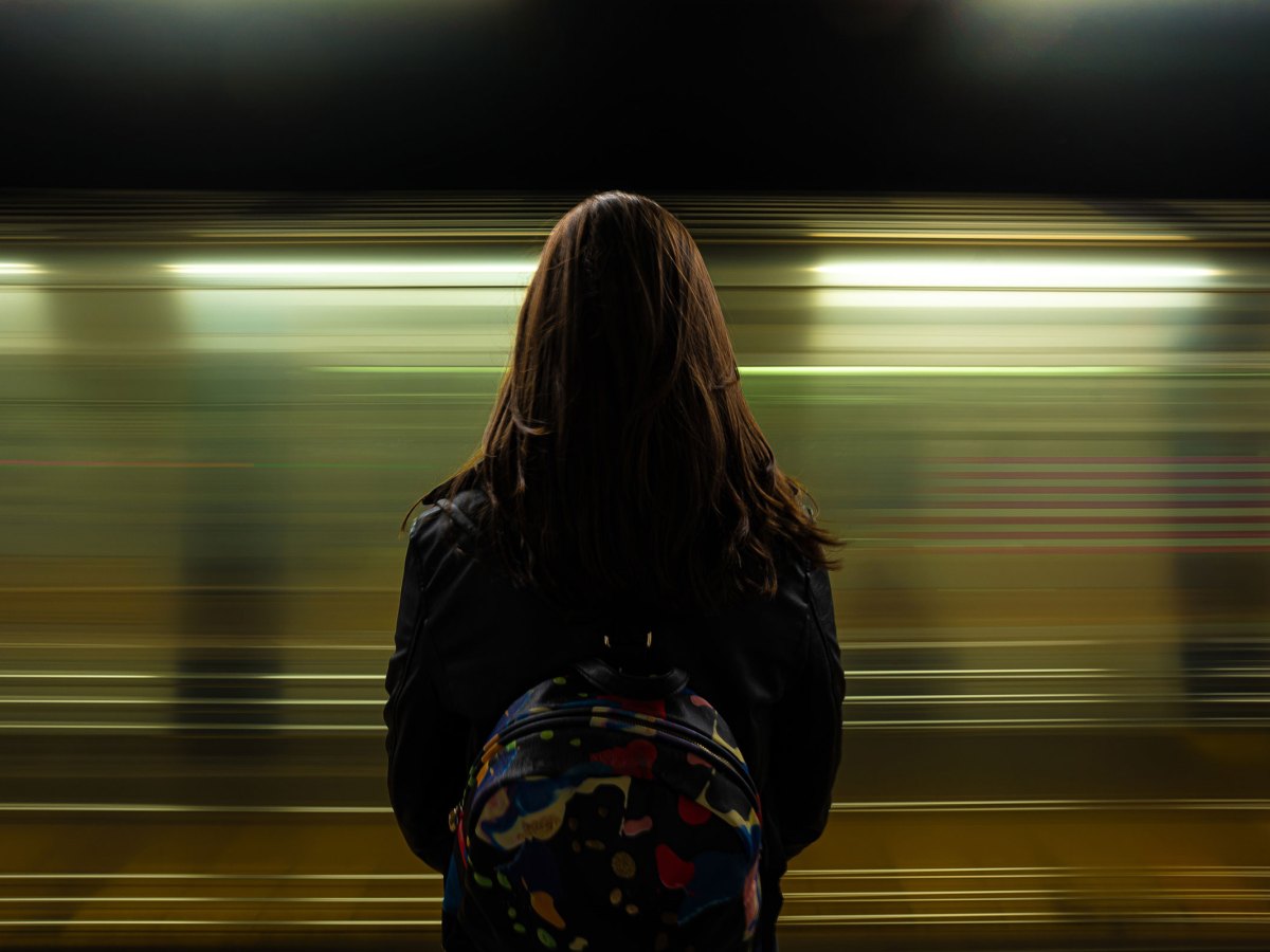 Frau steht am Bahngleis mit einem Rucksack