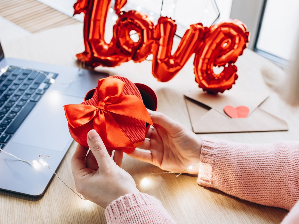 Frau, die vor ihrem Computer ein Geschenk in Herz-Form einpackt.