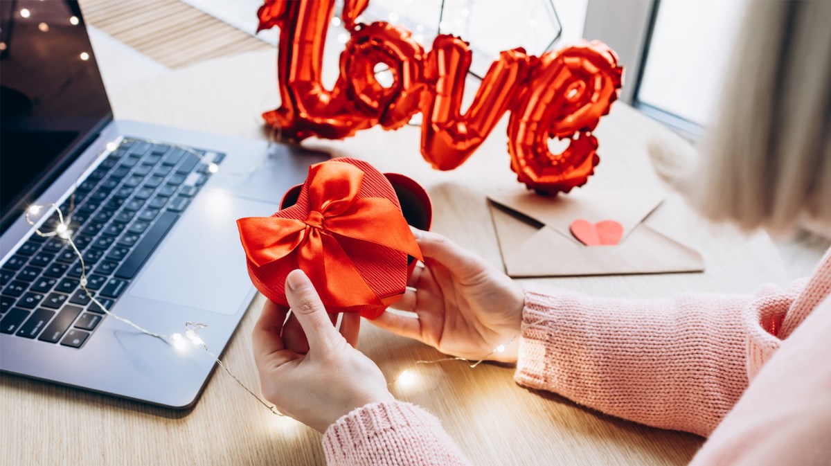 Frau, die vor ihrem Computer ein Geschenk in Herz-Form einpackt.