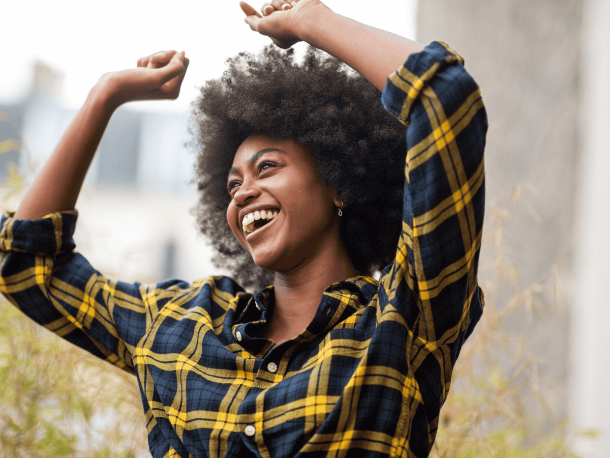 Frau mit kariertem Hemd und Armen in der Luft l&auml;chelt