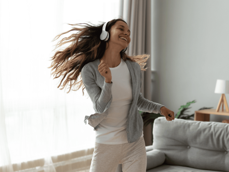 Frau mit Kopfhörern auf, lächelt und tanzt im Wohnzimmer