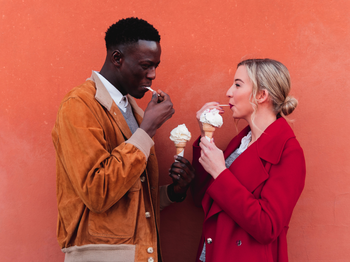 Ein Paar steht sich gegenüber vor einer orangen Wand und isst Eis
