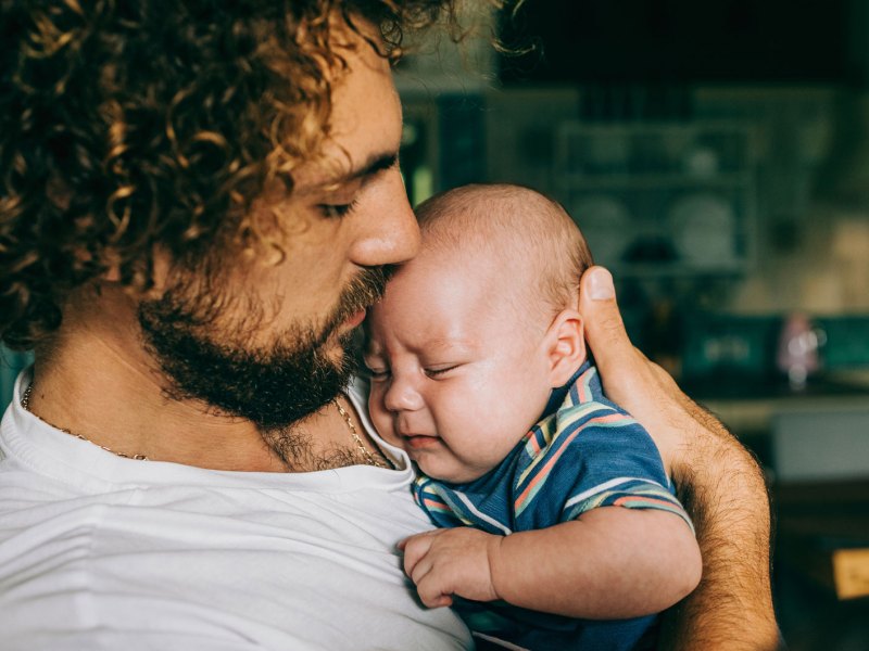 Vater h&auml;lt sein unzufriedenes Baby etwas hilflos auf dem Arm.